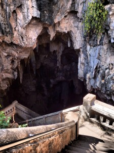 No matter where you go in the Phetchaburi province, all Wats seem to be filled with inquisitive monkeys. Khao Luang Cave is no exception to the rule. Located in Mueang Phetchaburi District, Phetchaburi, Khao Luang Cave is one of the largest in the region. The caves are set in Khao Luang hill which is almost 100 meters high. They consist of a number of caverns filled with beautifully illuminated golden Buddha images. King Mongkut (Rama IV) who's reign of the Kingdom started in 1851 until 1868, used the cave to study Buddhism and to meditate. Upon arriving at the foot of the hill, locals have put in place a barricade blocking the road up to the cave, thus enabling them to run a business charging 20THB to ferry you in a Tuk Tuk up the hill. Give it to the Thai's, if there's an opportunity no matter how sketchy, they will make money from tourists. From where you are dropped off, it's a short walk up a concrete staircase to the mouth of the cave. This pathway is home to many of the monkeys in the region, and taking care while walking is needed to ensure your own personal safety. Opting to purchase food at the bottom to feed the monkeys may just see you make the situation worse by encouraging many more to jump from the tree's in an effort to fill their belly's. As always, my biggest warning is to keep an eye out for the dominant male monkey, he will normally cause trouble if you are choosing to feed them. Walking down the steep stairs that lead into the cave, there is a strong smell of dank concrete and rock, but once you enter the main cavern, this smell subsides with the distraction of the sheer size of the cave. The cave is filled with Buddha images, several chedis and a great number of stalactites hanging from the ceiling. Also included is a Buddha image cast by order of King Chulalongkorn (Rama V). The atmosphere within the cave is serene and peaceful, it is a quiet place for reflection. Buddhist people will pay respect to the Buddha statues by burning candles and incense sticks. There are about 170 Buddha figures in Khao Luang cave. One of the most empowering is a large reclining Buddha, symbolizing the passing of the Buddha into final Nirvana. With the rays of the sun shining through holes in the ceiling, the caves are illuminated, giving the gold colored Buddha images a mystical appearance. You will also find rock like stalactites hanging from the caves ceiling, formed over the centuries by slow dripping water. Many of the caverns are lit by colourful florescent tubes, illuminating the walls in some surreal colours. How to get there: Khao Luang cave is located just North of Petchaburi, and a few kilometers away from Phra Nakhon Khiri historical park. The best way to get there is by private taxi or mini-bus. Time from Bangkok is around two hours, or shorter if you are coming from Hua Hin.